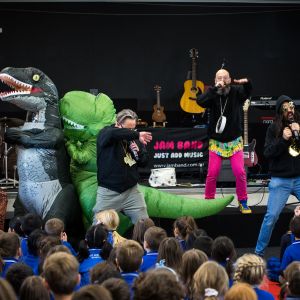 Jono Ruse and Nick Russell and Mark Curtis in costume and rapping next to big dinosaur costumes at a JAM Band performance in Adelaide South Australia